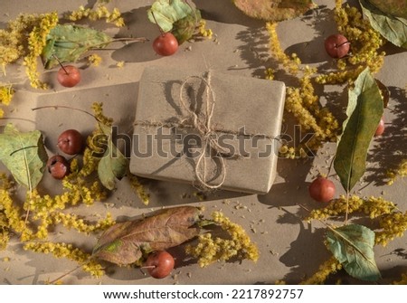 Autumn background idea. A gift in craft packaging surrounded by yellow flowers, dry leaves and apples. Autumn background. Eco friendly background. Autumn harvest. View from above.