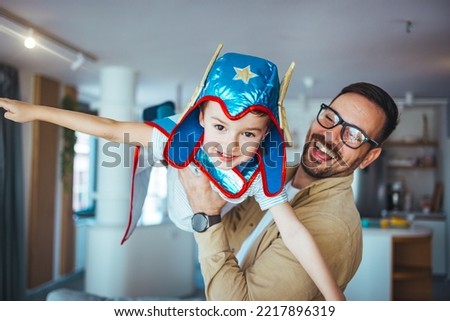 Dream big. Loving father helps his son fly like a superhero. Boy play fly with his dad at home. Cheerful familyare having fun together. Father holding son in superhero costume flying at home 