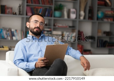 Male psychoanalyst sitting on sofa with clipboard.