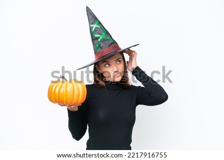 Young caucasian woman costume as witch holding a pumpkin isolated on white background having doubts and with confuse face expression