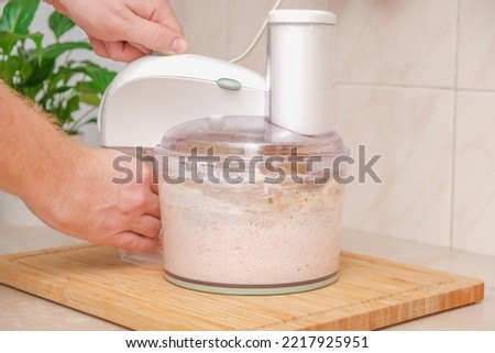 A man grinds pieces of chicken breast with spices, chicken egg, mayonnaise in a food processor. Meat puree in a food processor. The process of cooking chopped chicken cutlets. Royalty-Free Stock Photo #2217925951