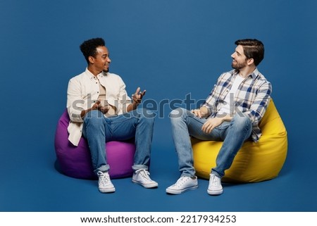 Full body young two friends happy fun cool cheerful men 20s wear white casual shirts together sit in bag chair talk speak isolated on plain dark royal navy blue background. People lifestyle concept Royalty-Free Stock Photo #2217934253