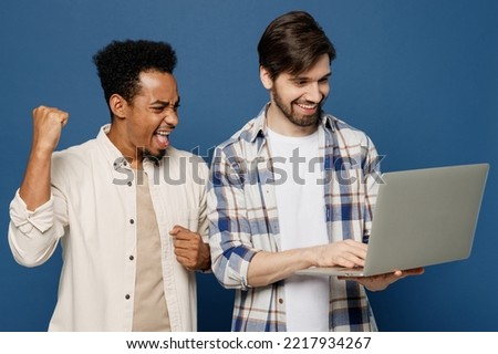 Young two friends overjoyed happy IT men wear white casual shirts together hold use work on laptop pc computer do winner gesture isolated plain dark royal navy blue background People lifestyle concept