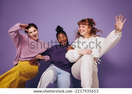 Energetic female friends dancing and having fun in casual clothing. Group of young women celebrating and having a good time against a studio background. Three best friends making cheerful memories.