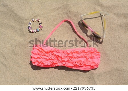 Sunglasses, bra and bracelet on sand, flat lay. Beach accessories