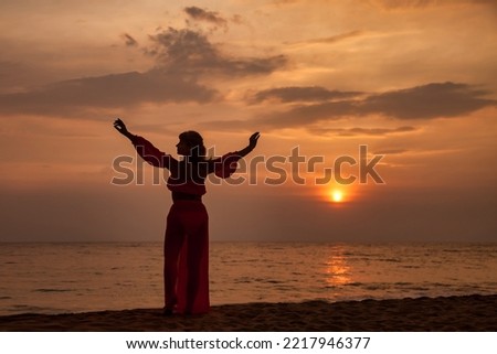 Silhouette middle aged woman arms raised posing on tropical sea sunset. Female relaxing on summer beach at tropical background. Lady in beachwear long dress. Travel vacation concept. Copy text space