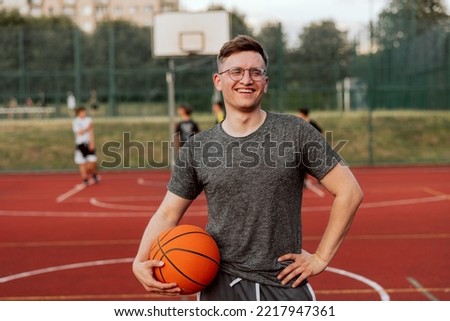 Basketball player delighted tired man in glasses holdig basketball ball posing during playing basketball game on the background friends training in sportswear. Company having fun outside.