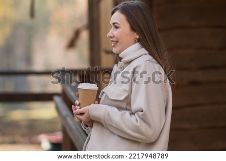 Young happy woman relaxing with hot tea or coffee on the cozy terrace of a wooden country house. Autumn cozy day. High quality photo