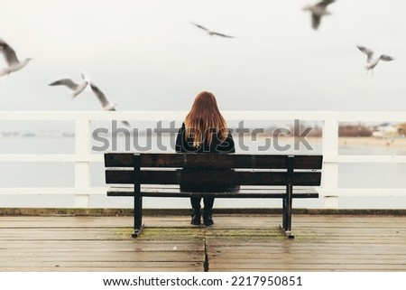 Woman sitting alone on bench by the sea. Gulls flying Royalty-Free Stock Photo #2217950851