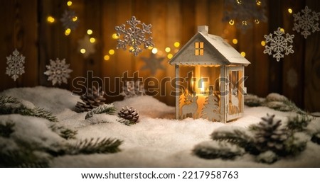 Christmas scene with lantern and hanging ornaments, wood background and snow, the burning candle and the brown planks create a cozy warm mood Royalty-Free Stock Photo #2217958763
