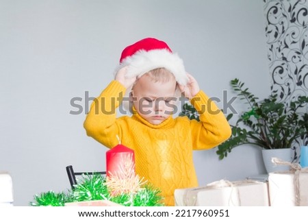 A cute little boy in a yellow sweater puts on a red Santa Claus hat. Celebrate Christmas and New Year.