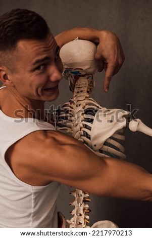 A man in a white T-shirt studies the structure of the human skeleton