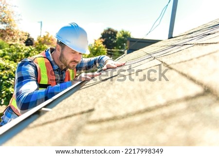 A man with hard hat standing on steps inspecting house roof Royalty-Free Stock Photo #2217998349