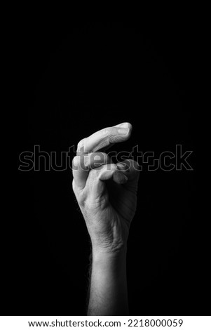 Dramatic black and white  image of a male hand fingerspelling the Japanese sign language letter 'RO' or 'ろ', isolated against a dark background with copy space.