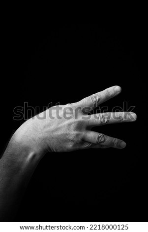 Dramatic black and white  image of a male hand fingerspelling the Japanese sign language letter 'MI' or 'み', isolated against a dark background with copy space.