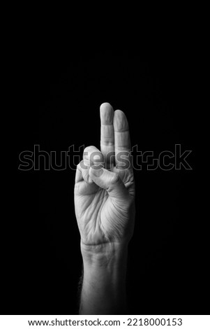 Dramatic black and white  image of a male hand fingerspelling the Japanese sign language letter 'U' or 'ぅ', isolated against a dark background with copy space.
