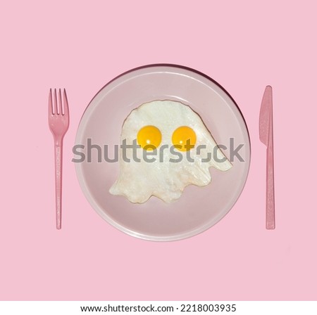 Pastel Halloween concept. Eggs forming ghost in plate on light pink background. Creative festive idea. Minimalistic holiday and food composition.