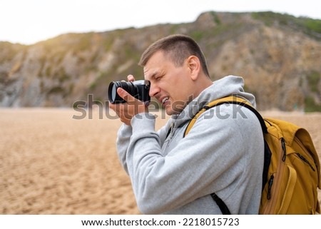 Traveler photographer takes photo beautiful seascape landscape on professional camera. Man tourist with backpack shoots a photo on beach. Side view middle shoot.
