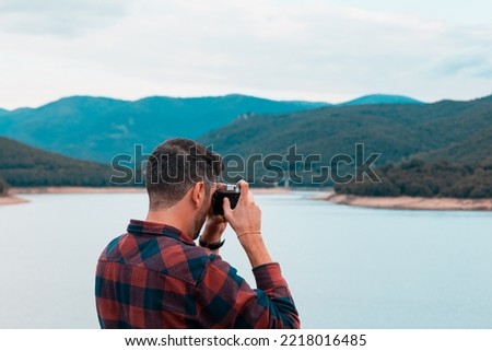 Back profile view of a photographer taking pictures at Lago di Gusana near Gavoi at sunset in autumn with dramatic clouds