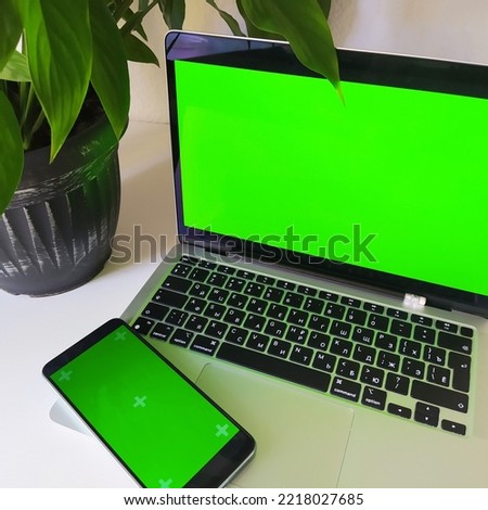 White table with two green screens included for copy: monitor and phone. Using a laptop with a mockup screen in the office, at home. Viewing, ordering on the Internet, online work, communication.