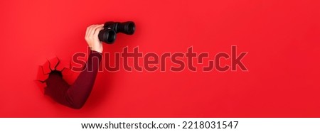 binoculars in hand over red background, panoramic layout Royalty-Free Stock Photo #2218031547