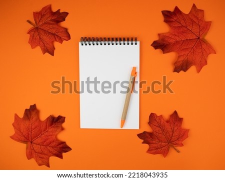 Autumn composition with blank notepad, pen and autumn leaves on orange background. Workplace. Flatlay. Top view. Copy space.