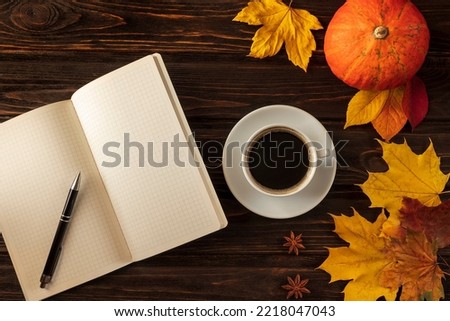 Concept of autumn office work or study. Coffee and notebook on a wooden table. Pumpkin and autumn leaves around. Copy space, flat lay