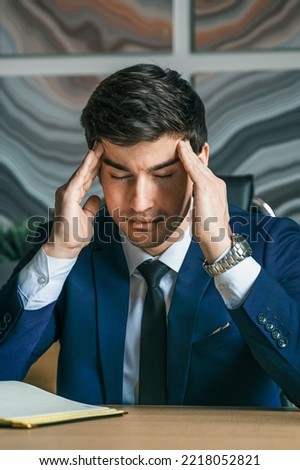 Stress and anxiety. Tired thinking businessman working with laptop in modern office. General manager,ceo. Young handsome confident man in suit sitting at table,workplace. Executive business career.