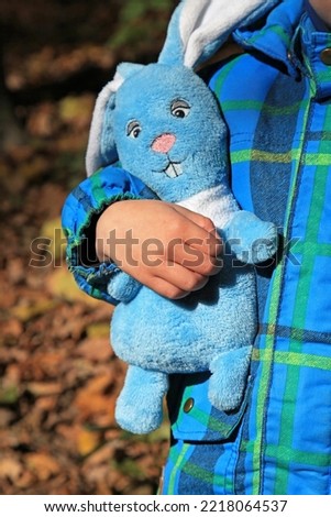 Favorite toy rabbit made of plush in the hand of a child in Autumn Park. Rabbit - a symbol of 2023 year according to the eastern calendar. New Year of 2023. Christmas, holidays, celebration concept