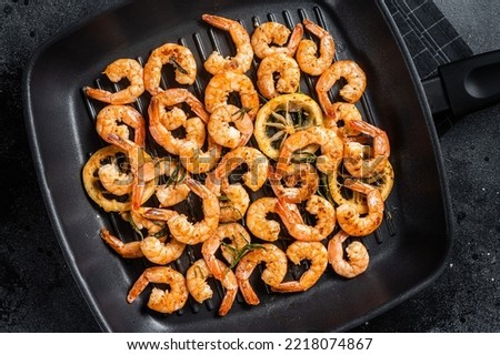 Roasted prawns shrimps with herbs on a grill skillet. Black background. Top view.