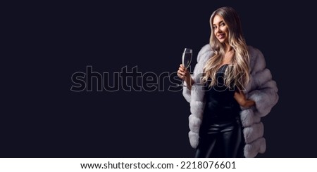 Beautiful gorgeous young blonde woman in fur coat holding champagne in hand stand while smiling celebrating something. 