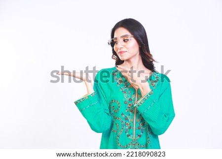 Portrait of a successful cheerful young Pakistani girl presenting something with her hand with a happy smiling face and looking at the empty copy space.