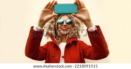 Portrait of happy smiling young woman taking selfie with smartphone wearing red jacket with fur hood