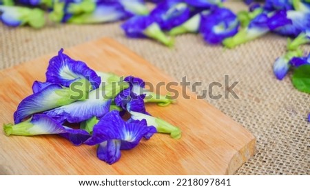 Selected focus Pile of butterfly pea flowers (Clitoria ternatea) on wodden board and burlap,  Telang flower for herbal tea raw materials - Photo product concept on photo studio with blur background
