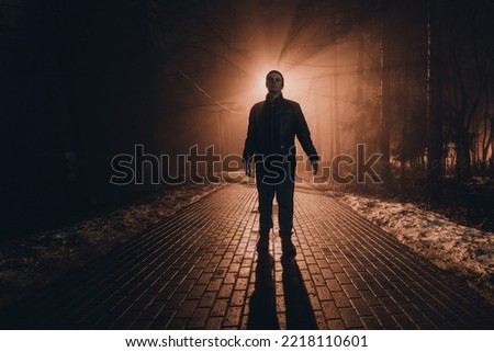 Sad man alone walking along the alley in night foggy park. Royalty-Free Stock Photo #2218110601