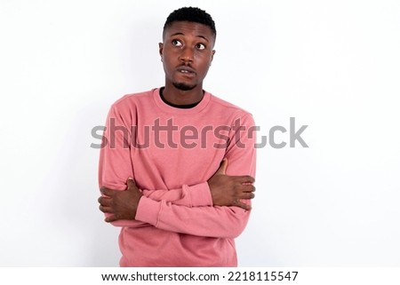 handsome man wearing pink sweater over white background bitting his mouth and looking worried and scared crossing arms, worry and doubt.