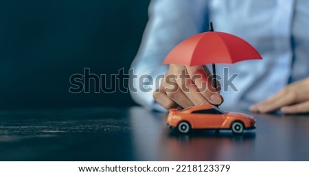 Mobile insurance concept. Umbrella on the car. Businessman holding umbrella and covering orange toy car on the table. Auto insurance, warranty, repair, finance, banking and money concepts.