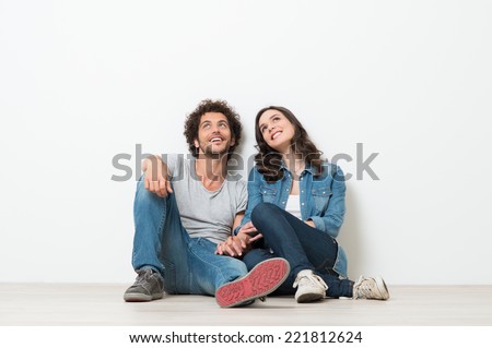 Portrait Of Happy Young Couple Sitting On Floor Looking Up Ready for your text or product