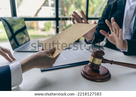 Businessman holding a cash envelope to bribe a participant's corrupt idea. lawyer gets money But he rejected the client's offer on a table with golden hammers and scales.