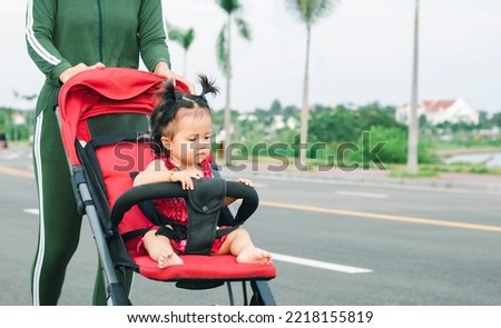 Full length of young mother pushing a stroller in the park. Young mom walking in park while pushing her toddler sitting in a stroller. High quality picture. Single mom concept. Copy space for text.