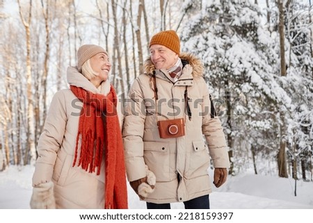 Waist up portrait of happy senior couple enjoying walk in winter forest and holding hands