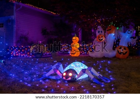 Glowing Halloween outdoor decorations with inflatable spider, pumpkins, ghosts and blue garlands in the house yard