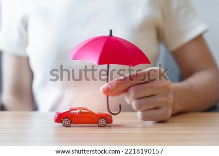 Businesswoman hand holding red umbrella and cover red car toy on table. Car insurance, warranty, repair, Financial, banking and money concept