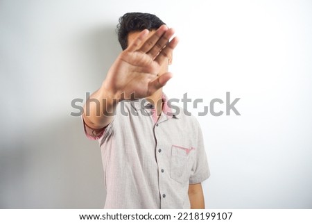 Attractive young asian man making fearful gestures with palms, defending himself from someone, asking to stop him immediately. Guy says stay away from me, show stop sign. Body language concept