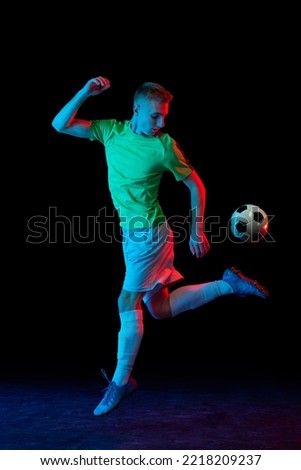 Leg kick. Young professional male football soccer player in motion and action isolated on dark background in neon light. Concept of sport, goals, competition, hobby, ad.