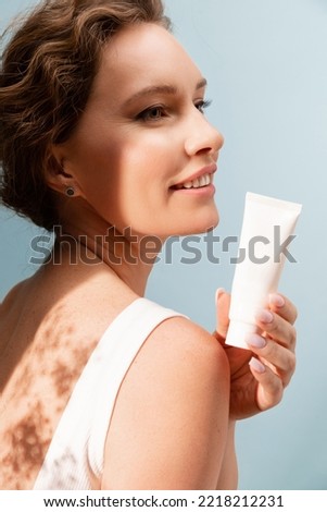 Portrait of a beautiful woman with a tube of sunscreen and moisturizer on a blue background