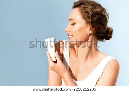 A beautiful smiling woman is holding a tube of moisturizer and sunscreen near her shoulders. Royalty-Free Stock Photo #2218212235