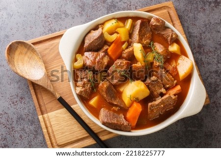Hearty Irish inspired beef stew made with garlic, stock, Guinness, bacon, potatoes, carrots, and onions closeup in the pot on the table. Horizontal top view from above

