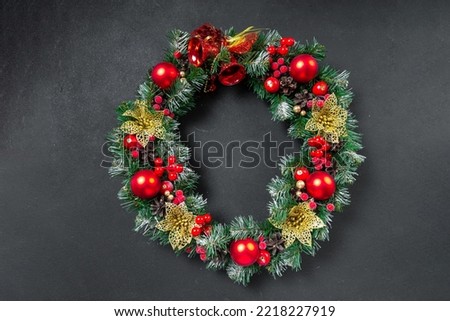 A Christmas wreath with a red bow and decorations of cones, holly, mistletoe, and winter greenery against a dark blue oak front door.