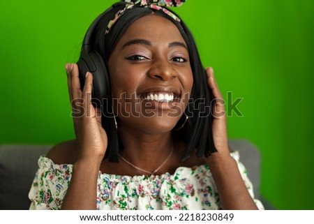 African woman listening to music with headphones while sitting on couch at home